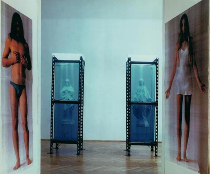 Robert Rumas, "Gesty" 1993, instalacja (dwa akwaria 210x60x60 cm, gipsowe figury Matki Boskiej i Jezusa, dwie fotografie kolorowe 130x60 cm, bielizna). Praca w depozycie Galerii Zderzak w Krakowie.